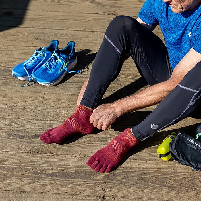 Injinji Mahogany no-show toe-separator socks on feet while tying running shoes.
